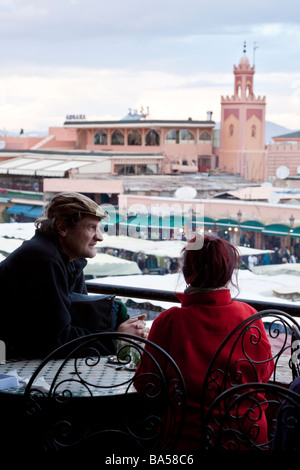 I turisti rilassarsi bevendo tè alla menta da una caffetteria con terrazza sul tetto che si affaccia sulla piazza Jemaa el Fna nella Medina di Marrakech Foto Stock