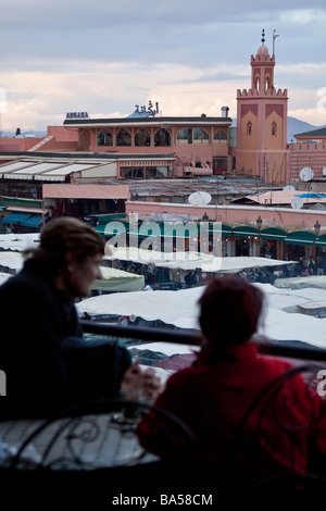 I turisti rilassarsi bevendo tè alla menta da una caffetteria con terrazza sul tetto che si affaccia sulla piazza Jemaa el Fna nella Medina di Marrakech Foto Stock