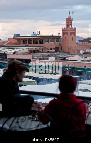 I turisti rilassarsi bevendo tè alla menta da una caffetteria con terrazza sul tetto che si affaccia sulla piazza Jemaa el Fna nella Medina di Marrakech Foto Stock