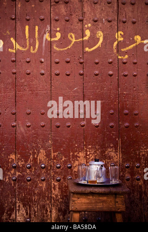 Tradizionale tè alla menta pronta per essere servita infront della storica porta con scritto a mano in arabo il souk Medina, Marrakech Foto Stock