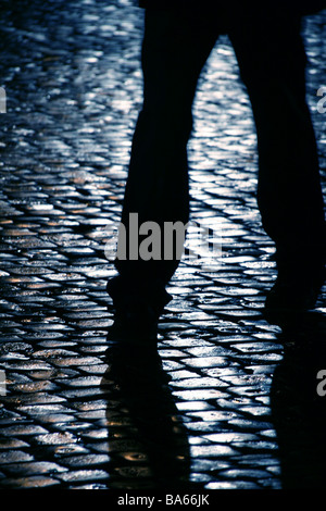 Persona che cammina sul bagnato strada di ciottoli di notte Foto Stock