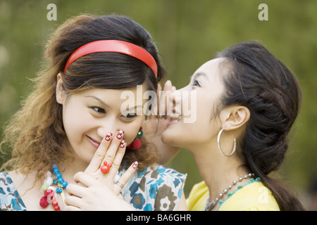 Una giovane donna whispering in altri s orecchio sorridente ritratto Foto Stock