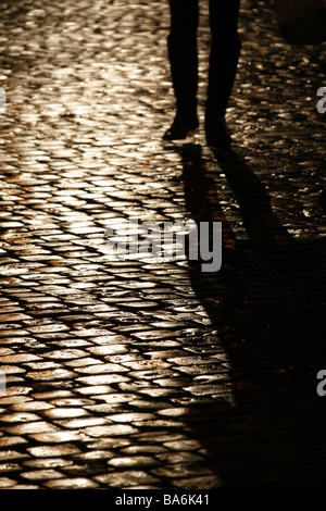 Persona che cammina sul bagnato strada di ciottoli di notte Foto Stock