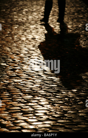 Persona che cammina sul bagnato strada di ciottoli di notte Foto Stock