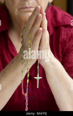 Una donna di mani stringendo un rosario durante la preghiera Foto Stock