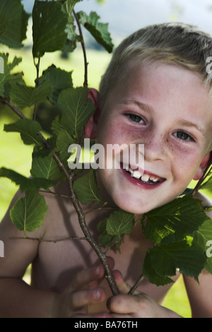 Dare nascita bionda ride faggio-branch detiene il ritratto di persone serie bambino di 5 anni lo sguardo di lentiggini fotocamera corpi superiore liberamente Foto Stock