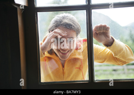 Donna che guarda attraverso una finestra in alp lodge, Heiligenblut, Parco Nazionale degli Hohe Tauern, Carinzia, Austria Foto Stock