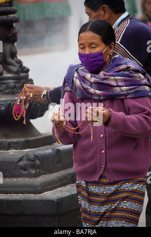 Donna Pellegrino con la maschera per il viso a Kathmandu Boudhanath pregando da statua e mulini di preghiera. Il Nepal Asia 90416 Nepal Foto Stock