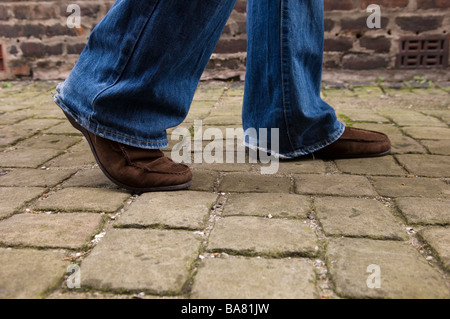 Close up di un uomo che indossa jeans e scarpe marrone a camminare in un vicolo urbano Foto Stock