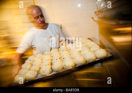 Un baker preparare calde tradizionali ciambelle trasversale per la pasqua UK - mettendo il greggio focacce cotte nel forno Foto Stock