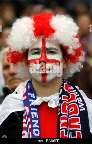 Un England Football fan con una faccia dipinta e indossa una parrucca colorata in gabbie prima di una partita Foto Stock