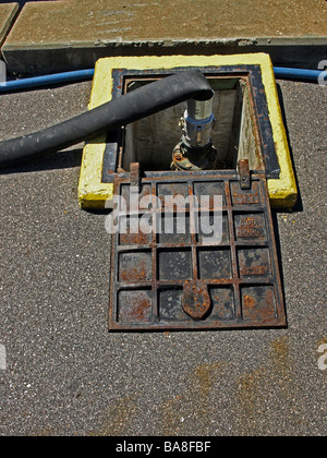 Tubo flessibile nero alimentazione in un connettore su una dock per combustibile o acqua o acque reflue per le navi con ferro porta aperta, giallo telaio di cemento Foto Stock