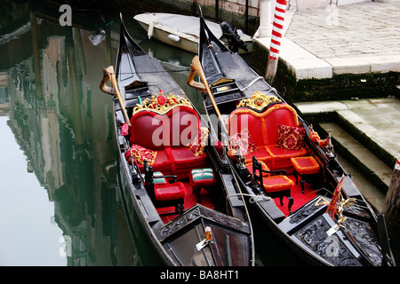 Due gondole con rosso sedi decorative, fianco a fianco su un canale con riflessi edifici veneziani Venezia Italia Foto Stock