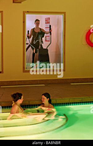 Due donne il bagno nella piscina e una donna che lavora fuori su un trainer ellittico nella zona fitness al Black Bear Resort. Foto Stock