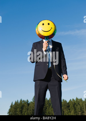 Imprenditore azienda Smiley face palloncino sulla faccia Foto Stock