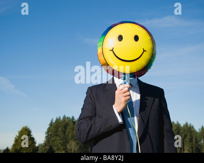 Imprenditore azienda Smiley face palloncino sulla faccia Foto Stock