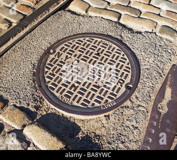 Coperchio di fognatura su strada urbana Foto Stock