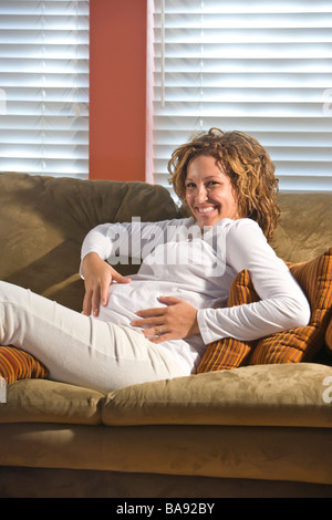 Incinta donna afro-americana sdraiata su un divano Foto Stock