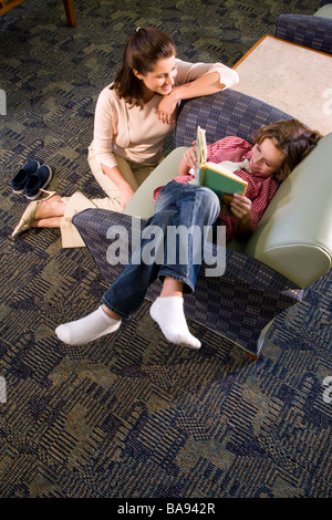 Insegnante di scuola elementare con pupilla nella libreria in poltrona Foto Stock