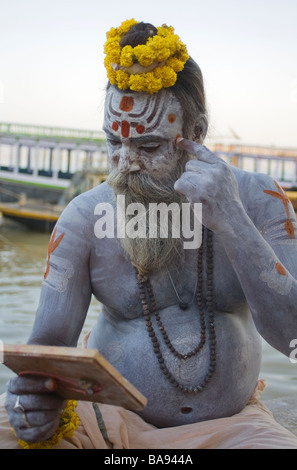 Un indiano Saddhu coperto di cenere faccia applicare vernice a Varanasi, India Foto Stock