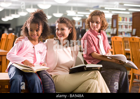 Insegnante di scuola elementare seduta con gli alunni in biblioteca Foto Stock