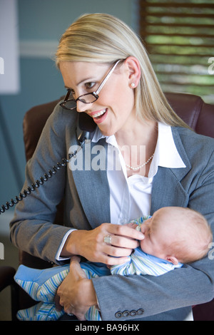 Giovane imprenditrice azienda baby sul lavoro e sul telefono Foto Stock