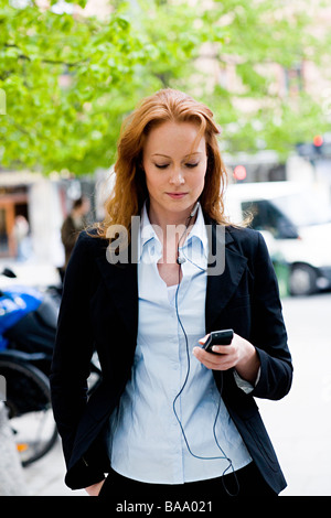 Donna in piedi all'aperto con auricolare e un cellulare, Stoccolma, Svezia. Foto Stock