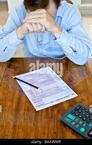 Uomo anziano con macchie di età sulle mani con noi Tassa federale forma sul tavolo di legno con la matita e calcolatrice Foto Stock
