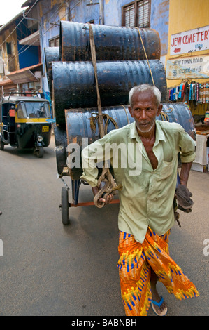 Commerciante di strada che trasporta tamburi di olio di cocco da un deposito a stallo in Old Kochi's (Cochin) zona delle spezie, Kerala, India Foto Stock