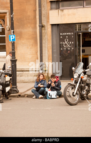 Una giovane coppia di studenti seduti sul marciapiede e mangiare, Broad Street, Oxford Foto Stock