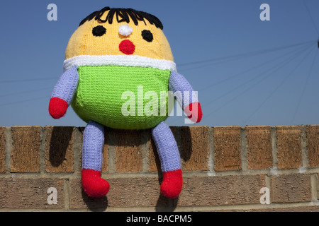 Un Humpty Dumpty giocattolo morbido sat sul muro con un cielo blu sullo sfondo. Foto Stock