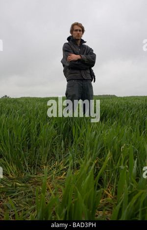 Un giovane uomo che indossa un nero giacca di pelle sorge in un campo verde Foto Stock