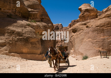 Un cavallo e un carrello che porta i turisti galoppa attraverso il Siq stretta gola nel Nabatean antica città di Petra in Giordania Foto Stock
