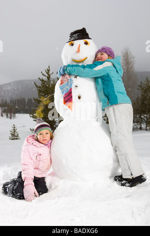 Ragazze abbracciando pupazzo di neve, vicino a Frisco, Summit County, Colorado, STATI UNITI D'AMERICA Foto Stock