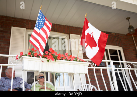 Coppia senior sul portico anteriore con American e bandiere canadesi Foto Stock