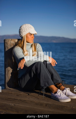 Donna seduta sul dock dal lago Foto Stock