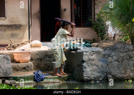 Keralan donna lavaggio vestiti in fiume fuori casa di famiglia nel Backwaters, Kerala, India meridionale Foto Stock