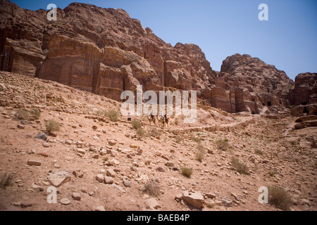 I turisti sui cammelli ingaggiato ride passato Royal Nabataean tombe scavate nella pietra arenaria della città antica di Petra, Giordania Foto Stock