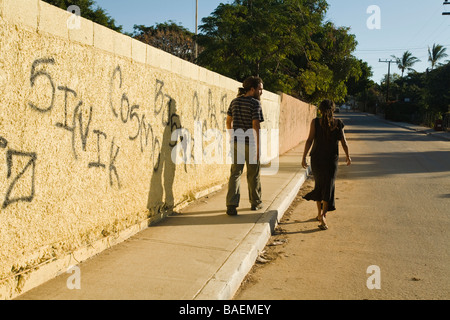Messico La playita giovane adulto giovane a piedi passato graffiti dipinti con vernice a spray nera sulla parete gialla nella piccola città del Messico Foto Stock