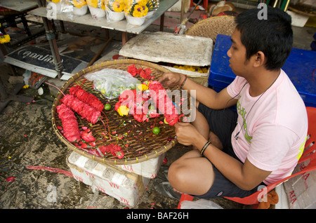 Un uomo tailandese fare ghirlande di fiori al di fuori di un tempio indù a Bangkok in Tailandia Foto Stock