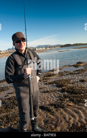 Un pescatore in vacanza pesca sportiva nel Menai Straits Anglesey north Wales con Caernarfon town e il castello di background REGNO UNITO Foto Stock