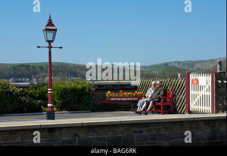 Coppia di anziani seduti su una panchina a Settle stazione ferroviaria, North Yorkshire, Inghilterra, Regno Unito Foto Stock