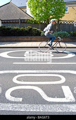 British indicazioni stradali che indicano un 20 miglia per ora limite di velocità, con passaggio di ciclista non usando le mani Foto Stock