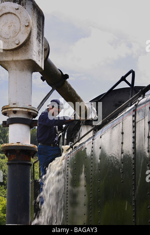 Un treno a vapore tenendo in acqua il serbatoio trabocca e l'ingegnere spostando il braccio d'acqua lontano Limousin Francia Foto Stock