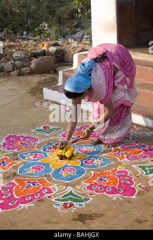 Donna indiana mettendo i bastoncini di incenso in un'offerta di fiori e di sterco di vacca su un Rangoli design in un Indiano street Foto Stock