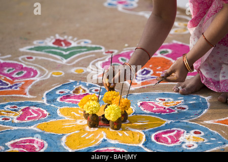 Donna indiana mettendo i bastoncini di incenso in un'offerta di fiori e di sterco di vacca su un Rangoli design in un Indiano street Foto Stock