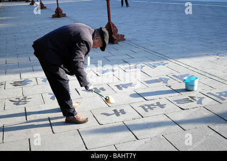 Il vecchio uomo cinese praticare la calligrafia acqua con una spazzola. Una visione comune in parchi e spazi pubblici in Cina. Foto Stock