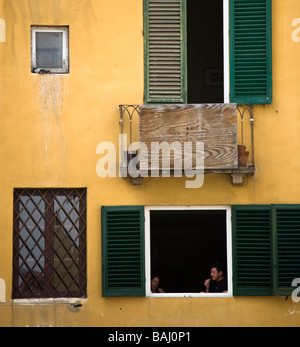Un giovane seduto a pranzo in una finestra shutterd in Piazza Anfiteatro, Luca, Toscana, Italia Foto Stock