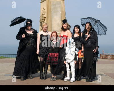 Un gruppo di donne e bambini vestiti da goti pongono davanti a James cuochi statua alla biennale festival Goth a Whitby Foto Stock