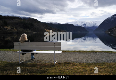 Donna seduta su una panchina godendo la vista, Hardangerfjord, Norvegia Foto Stock